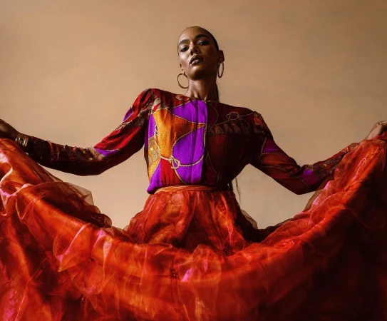 Model in colourful patterned blouse and voluminous red skirt holding the fabric edges in a low-angle shot.