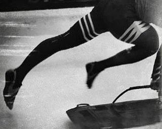 Monochrome image of a bobsledder in motion, showcasing their legs and the bobsled, emphasizing the speed and sport of bobsleighing.