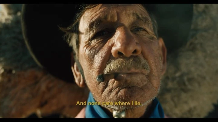 Close up of an elderly man with a cigar, a mustache, and wrinkles on his face wearing a blue bandanna around his neck outside.
