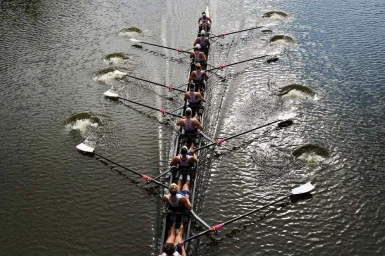An overhead action shot of a crew team rowing an eight-person racing shell along a river in New York, captured by Andy Anderson.