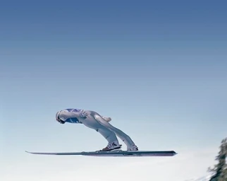 Ski jumper soaring through the clear blue sky in an aerodynamic forward-leaning position on skis