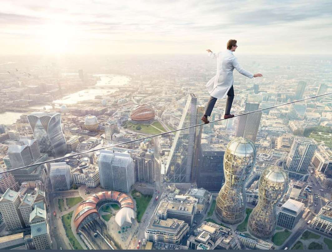 A person in a lab coat is walking on a tightrope strung across a city skyline with tall buildings and a bright sky above.