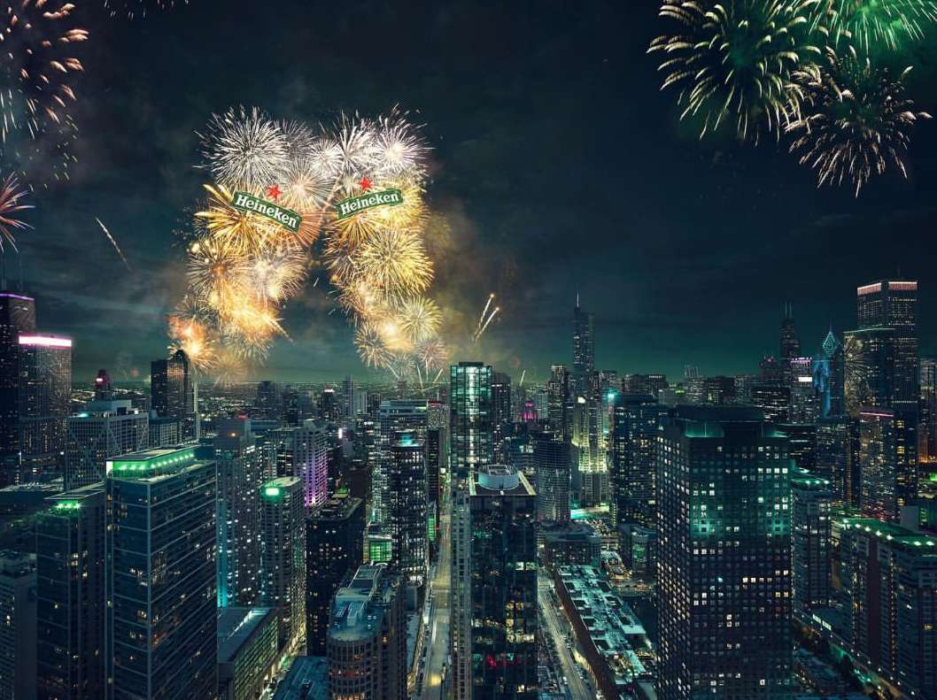 Cityscape at night with fireworks and Heineken logos in the sky, viewed from above, showcasing an urban celebration.