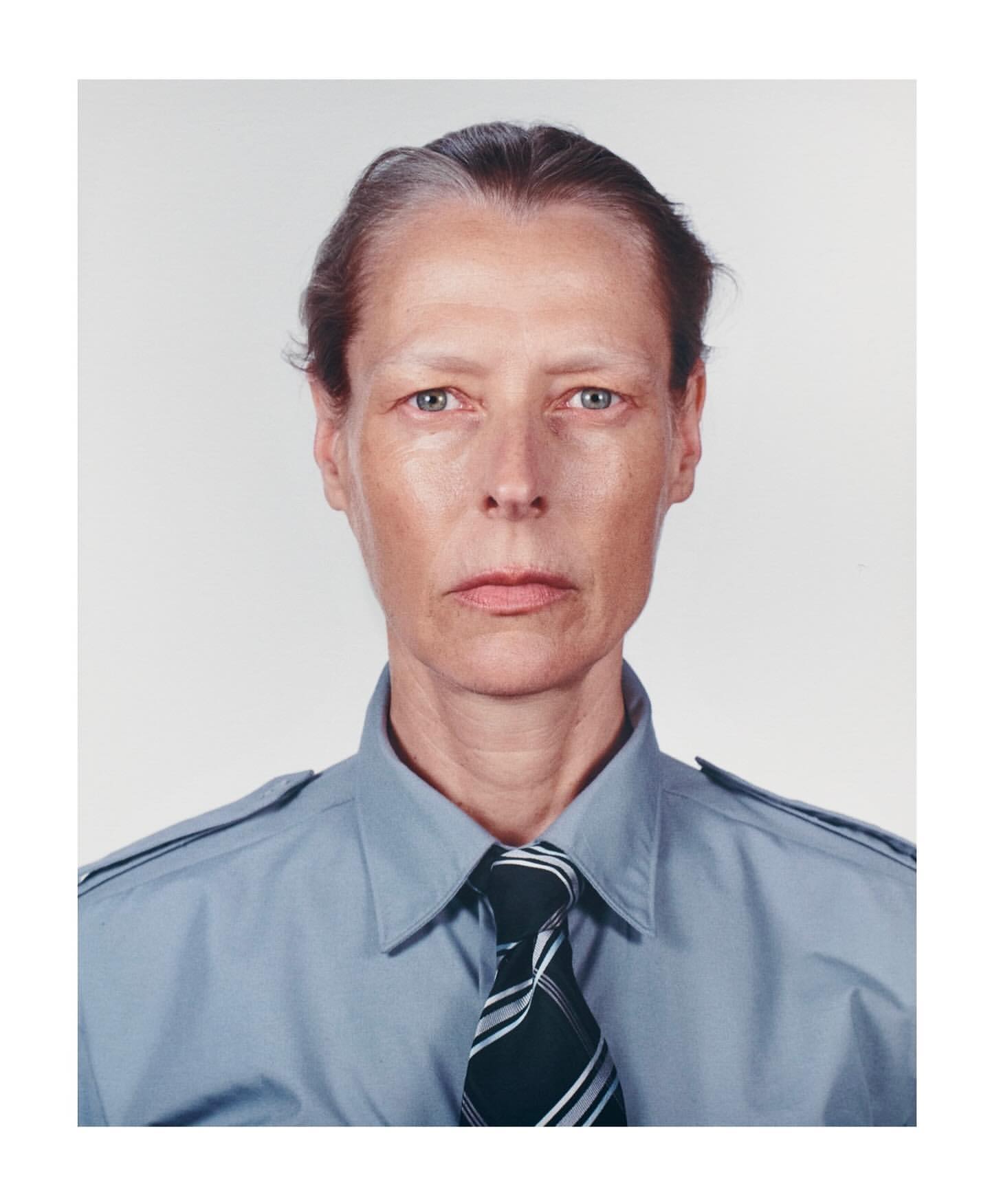 Portrait of an adult female with short grey hair wearing a blue collared shirt and tie, captured in a photo studio setting with soft lighting.