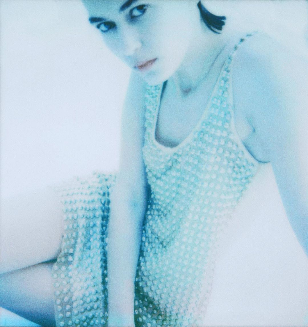 Young woman with short dark hair in beaded dress posing in a hazy, low-contrast photo studio environment with predominantly blue tones.