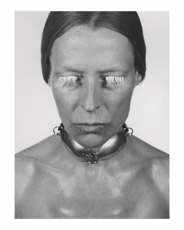 Monochrome portrait of a woman with exaggerated white eyelashes and a wide metal collar, set against a neutral background.