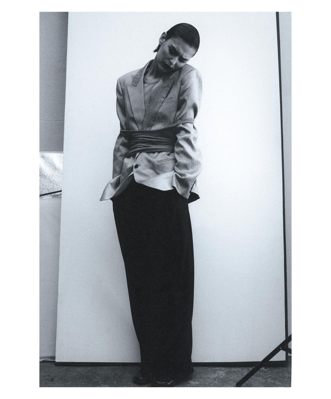 A woman in a blazer and long skirt poses in front of a white background in a black and white fashion shot with high contrast.