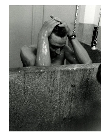 Black and white portrait of an adult male sitting in a bathtub, holding his head, photographed indoors with a close-up camera angle.