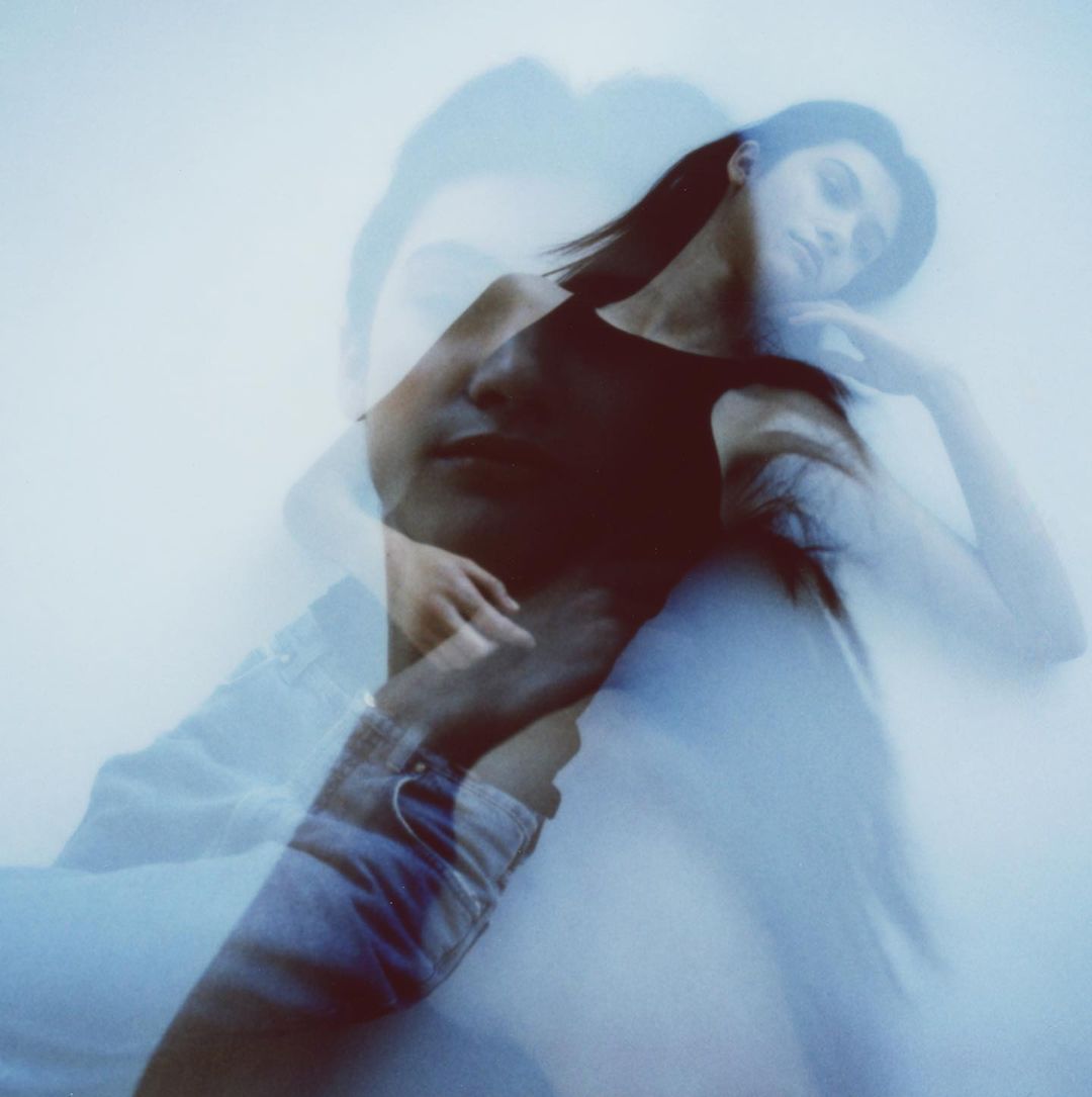 Multiple exposure image of a woman wearing a black tank top and denim shorts against a soft, light blue background in a photo studio.