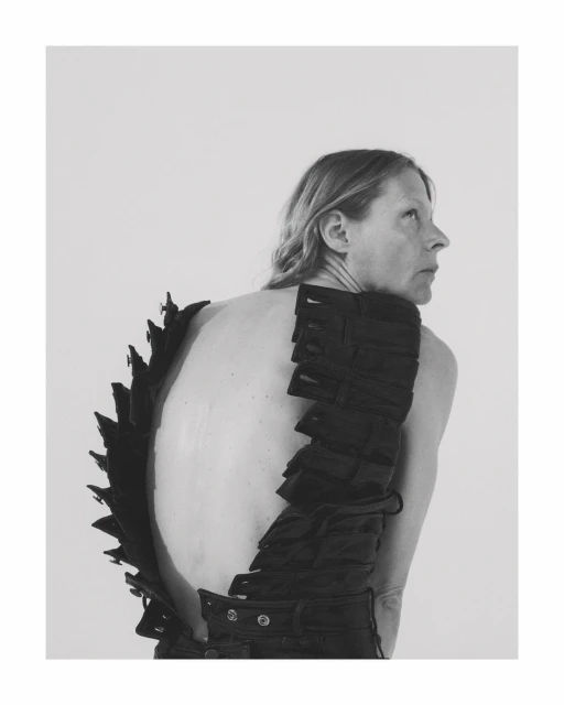 Monochrome portrait of an adult woman with bare back wearing a black textured garment and looking sideways in a bright photo studio.