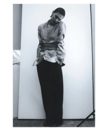 Monochrome portrait of a model standing against a white backdrop, wearing an oversized blazer cinched at the waist.