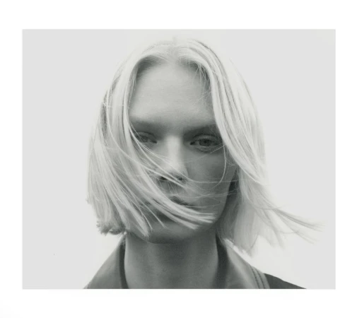 Close-up portrait of a blonde model with hair blowing across face against a plain light background by Andy Harrington