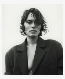 Portrait of a woman with dark wavy hair and a structured black blazer against a plain white background by Andy Harrington