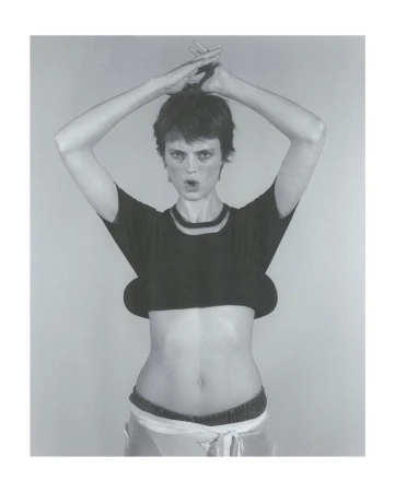 Monochrome portrait of a woman with short dark hair holding her hands above her head in front of a grey studio background