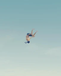 A man is captured mid-air executing a flip against a clear light blue sky background.