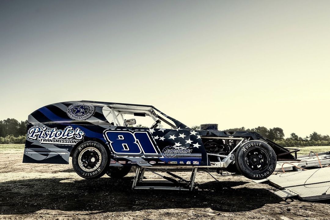 Race car number 81 on a lift outdoors under a bright, clear sky. The vehicle is detailed with brand logos and American flag motif.