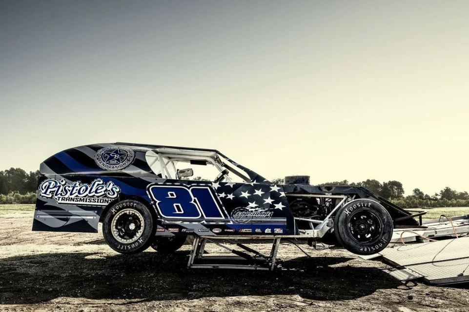 Race car number 81 on a lift outdoors under a bright, clear sky. The vehicle is detailed with brand logos and American flag motif.
