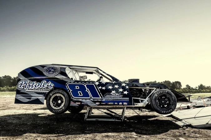 Race car number 81 on a lift outdoors under a bright, clear sky. The vehicle is detailed with brand logos and American flag motif.