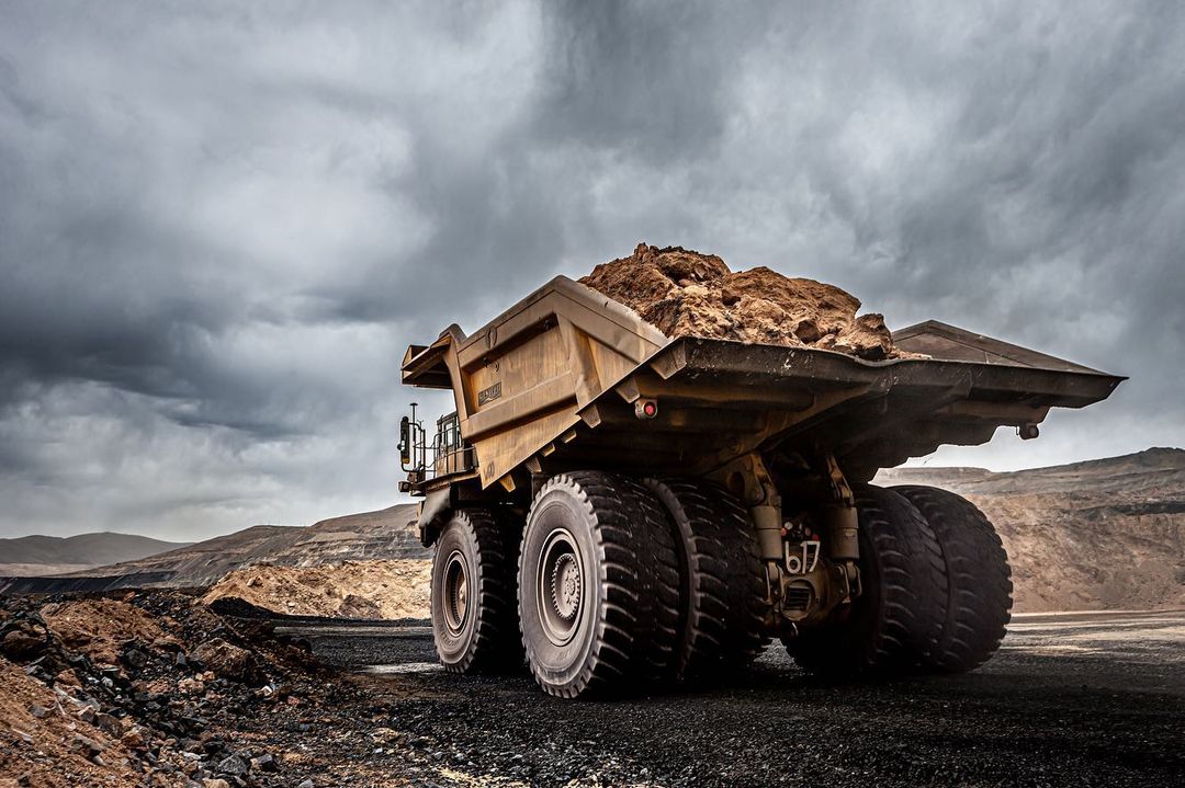 Heavy-duty dump truck filled with earth on a gravel road with a cloudy sky and desert landscape in the background. Mining industry theme.