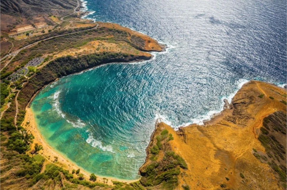 Aerial view of Hanauma Bay, Oahu, Hawaii featuring a turquoise lagoon, beach, volcanic coastline, and Pacific Ocean's deep blue waters.