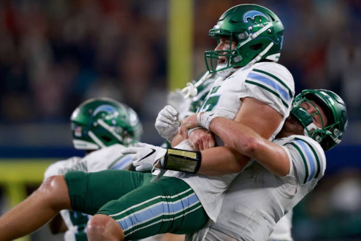 Two football players in green and white uniforms embrace on the field after a game, showcasing the joy of sportsmanship and teamwork.