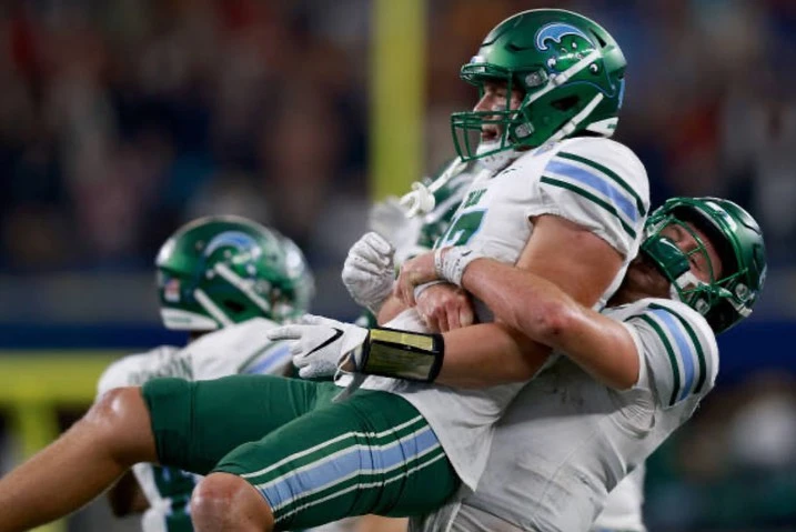 Two football players in green and white uniforms embrace on the field after a game, showcasing the joy of sportsmanship and teamwork.