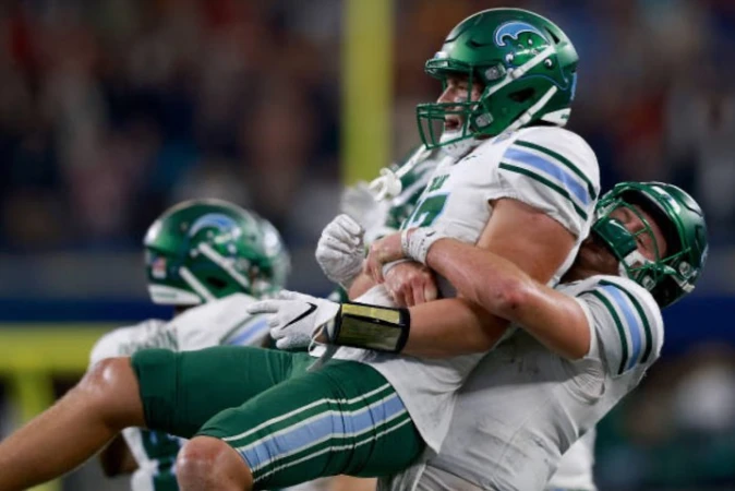 Two football players in green and white uniforms embrace on the field after a game, showcasing the joy of sportsmanship and teamwork.