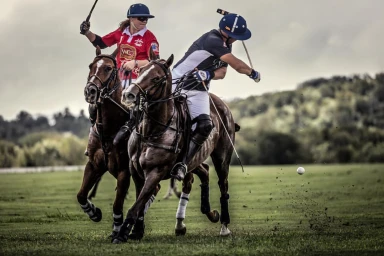 Two polo players on horses riding across a grassy field, photographed by Andy Mahr.
