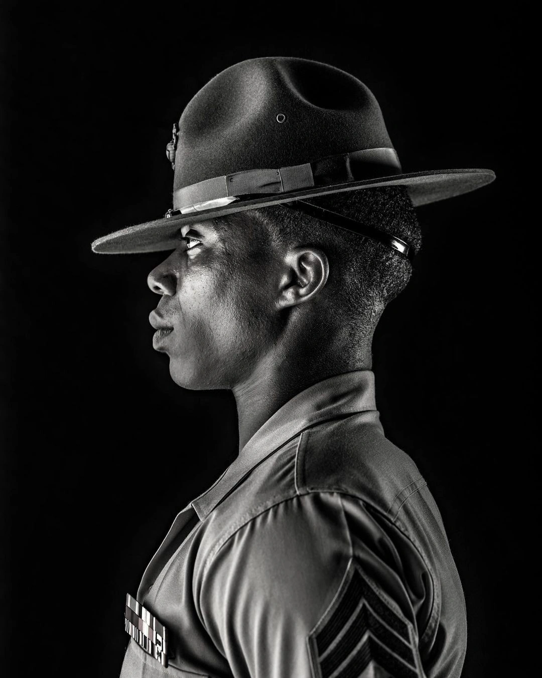 Black man in profile wearing a military campaign hat and uniform against a stark dark background
