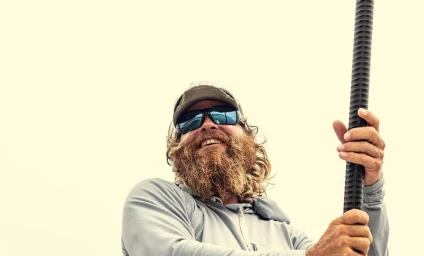 Bearded man in sunglasses and baseball cap holding a ridged pole against a bright sky, photographed by Andy Mahr.
