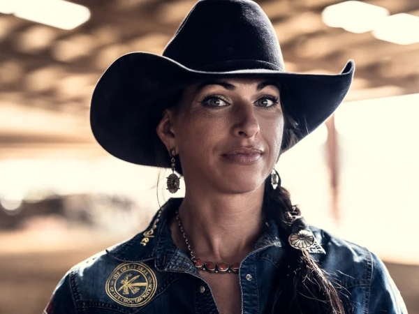 Close-up portrait of a woman wearing a black cowboy hat, denim shirt, and decorative necklace.