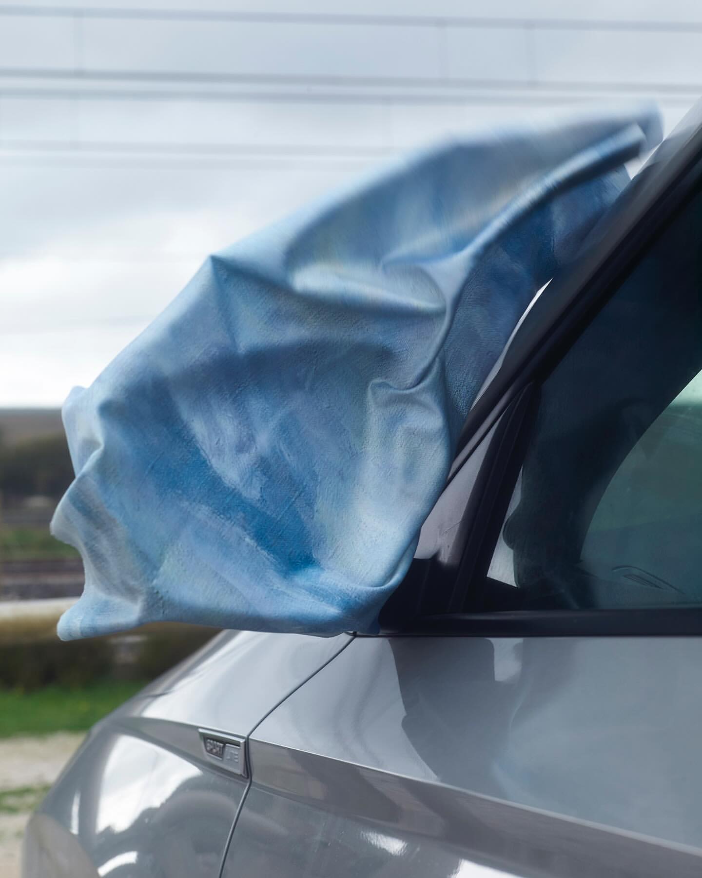 Car with a blue and white fabric covering the side mirror, parked outdoors. Close-up shot of vehicle and fabric.