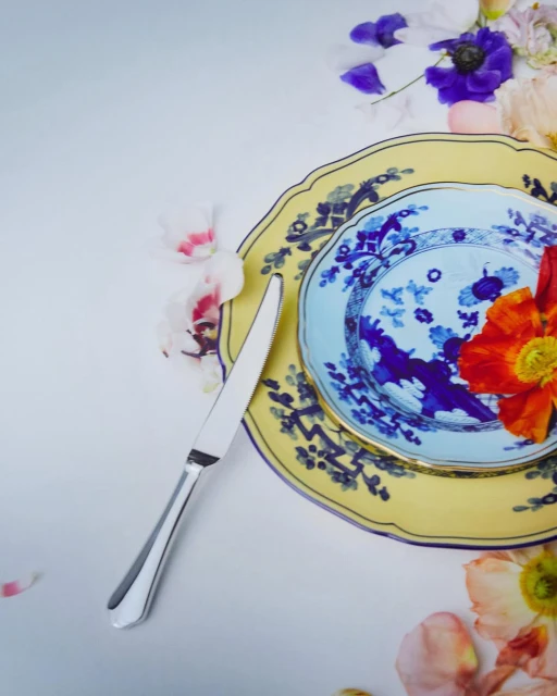 Overhead shot of decorative plates, silverware, and floral accents on a white surface, capturing an elegant and artistic food presentation.