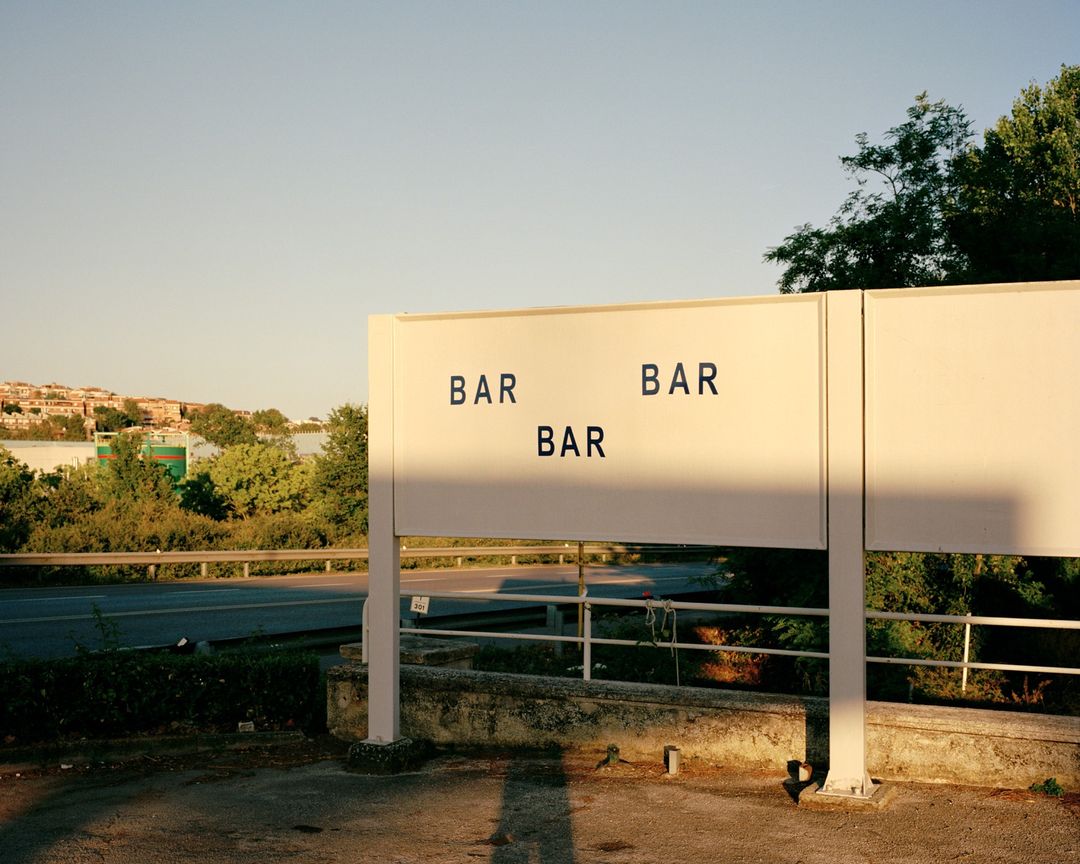 Outdoor sign with 'BAR' repeated against a backdrop of urban landscape and clear sky, creating a conceptual, minimalist visual.