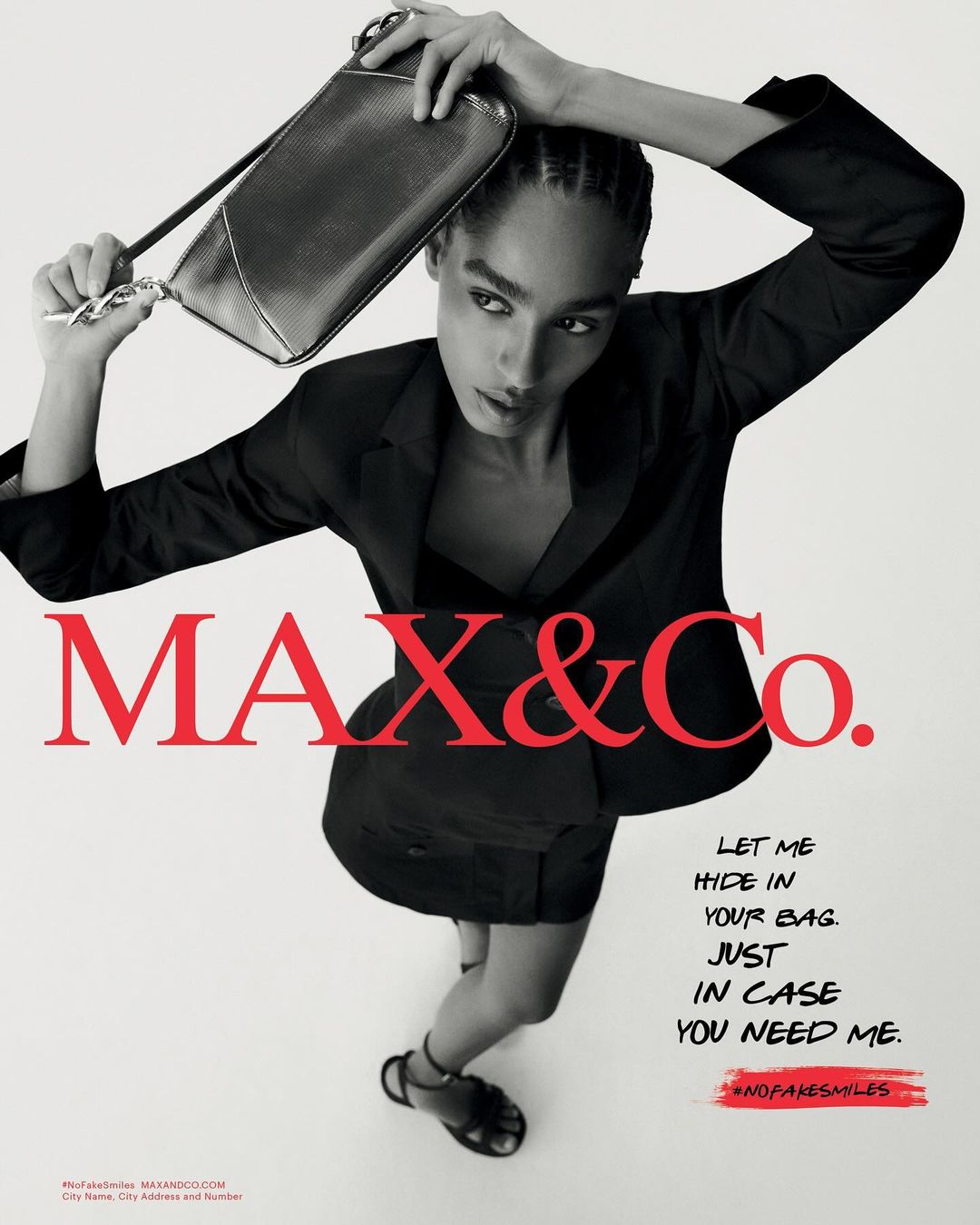 Black and white fashion advertisement for Max&Co. features an adult woman in a dark suit holding a shiny clutch overhead.