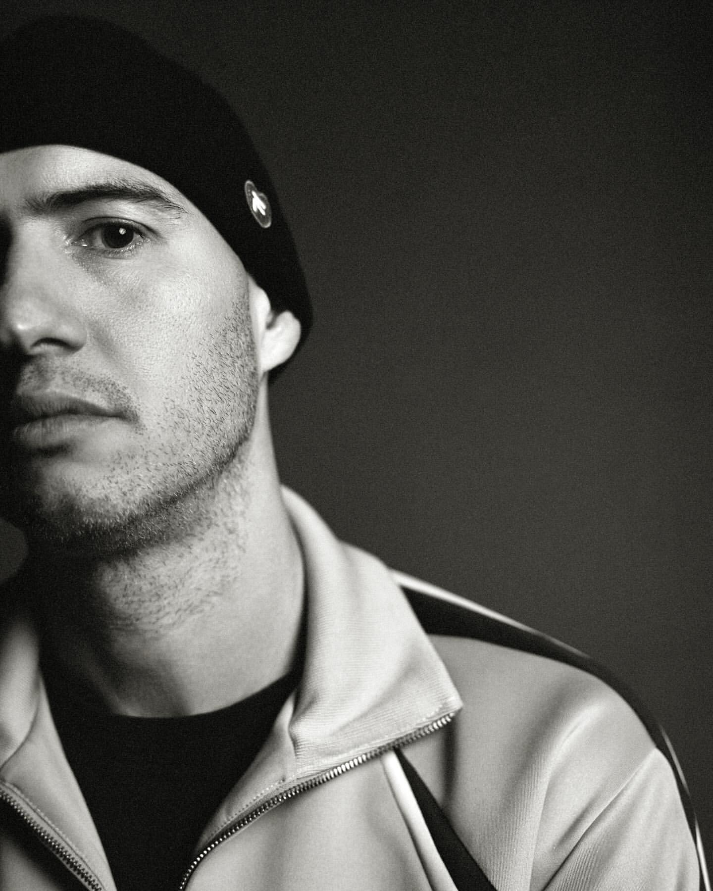 Close-up monochrome portrait of a man wearing a black beanie and track jacket by Andy Massaccesi in Milan.