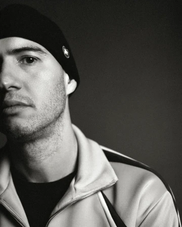 Close-up monochrome portrait of a man wearing a black beanie and track jacket by Andy Massaccesi in Milan.