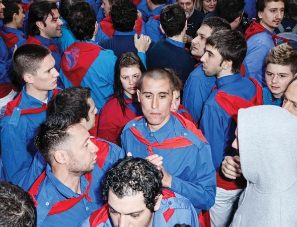 Large group of adult males, most wearing matching blue collared shirts with red scarves, gathered indoors. Crowd of people. 
