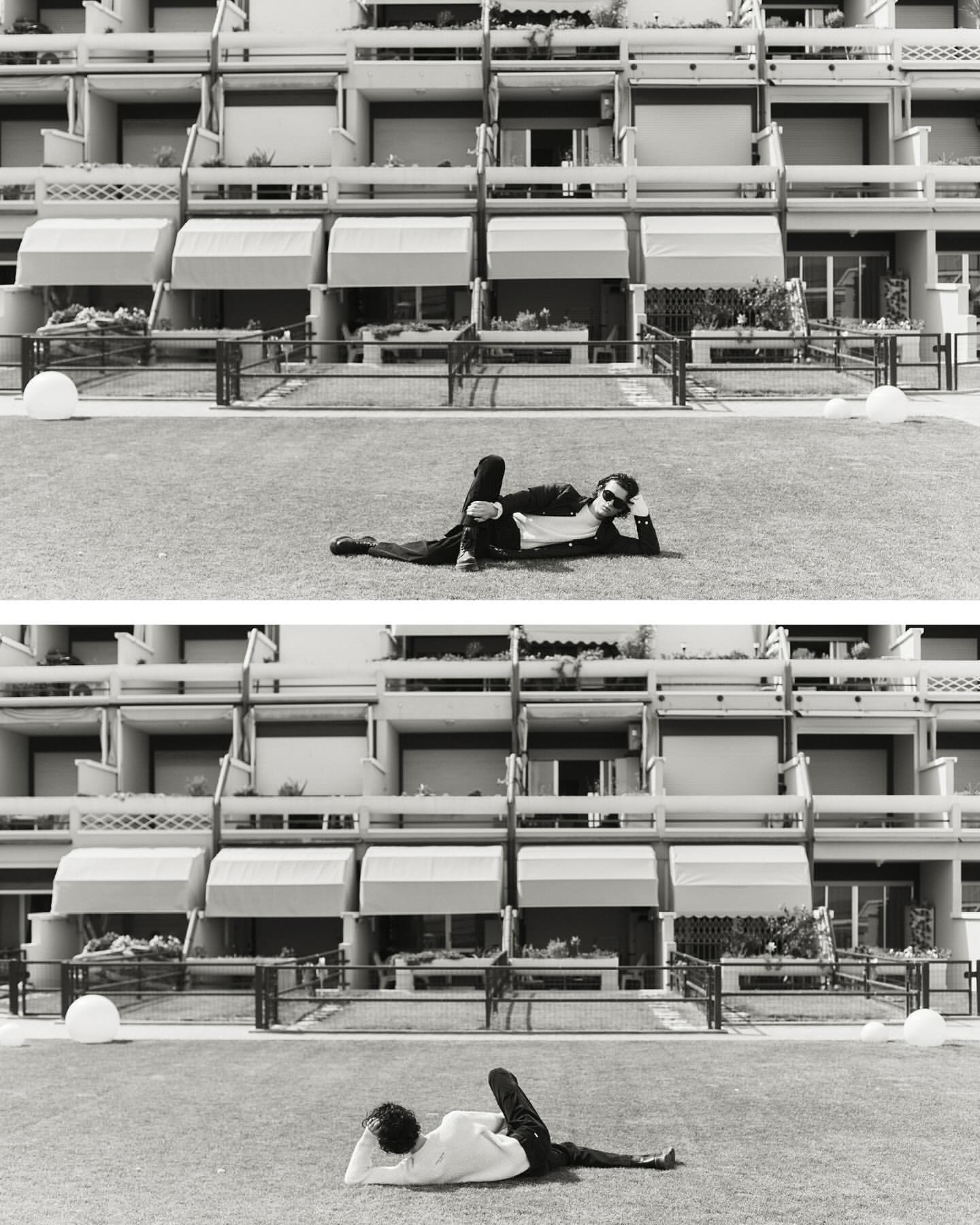 Split-frame black and white editorial image of a person reclining on grass in front of a multi-story residential building facade.