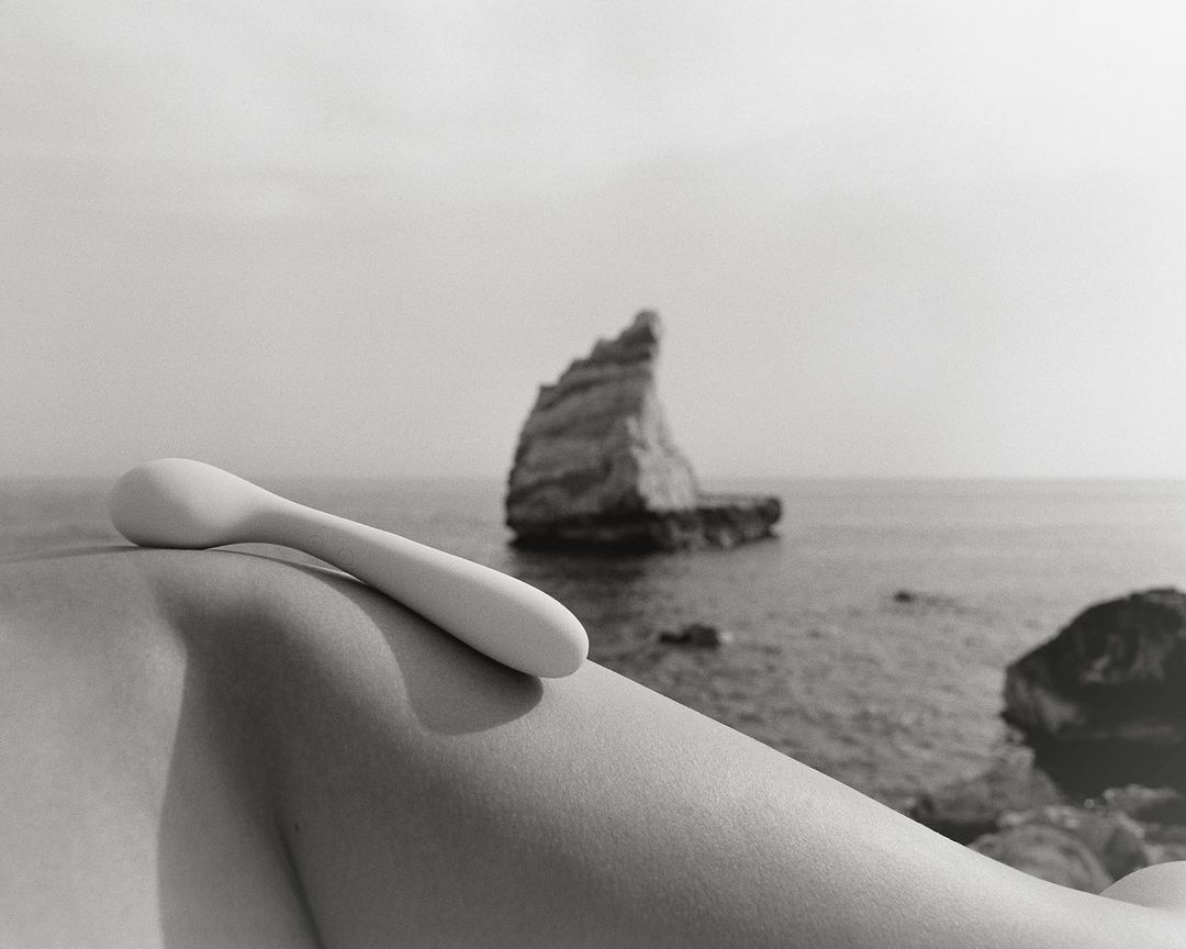 Monochrome shot of a person's arm with a white implement against a sea backdrop featuring a rocky island and overcast sky.