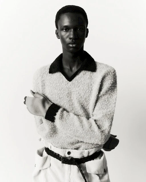 Portrait of a Black male model in a fuzzy sweater and corduroy pants against a bright white backdrop in a studio setting.