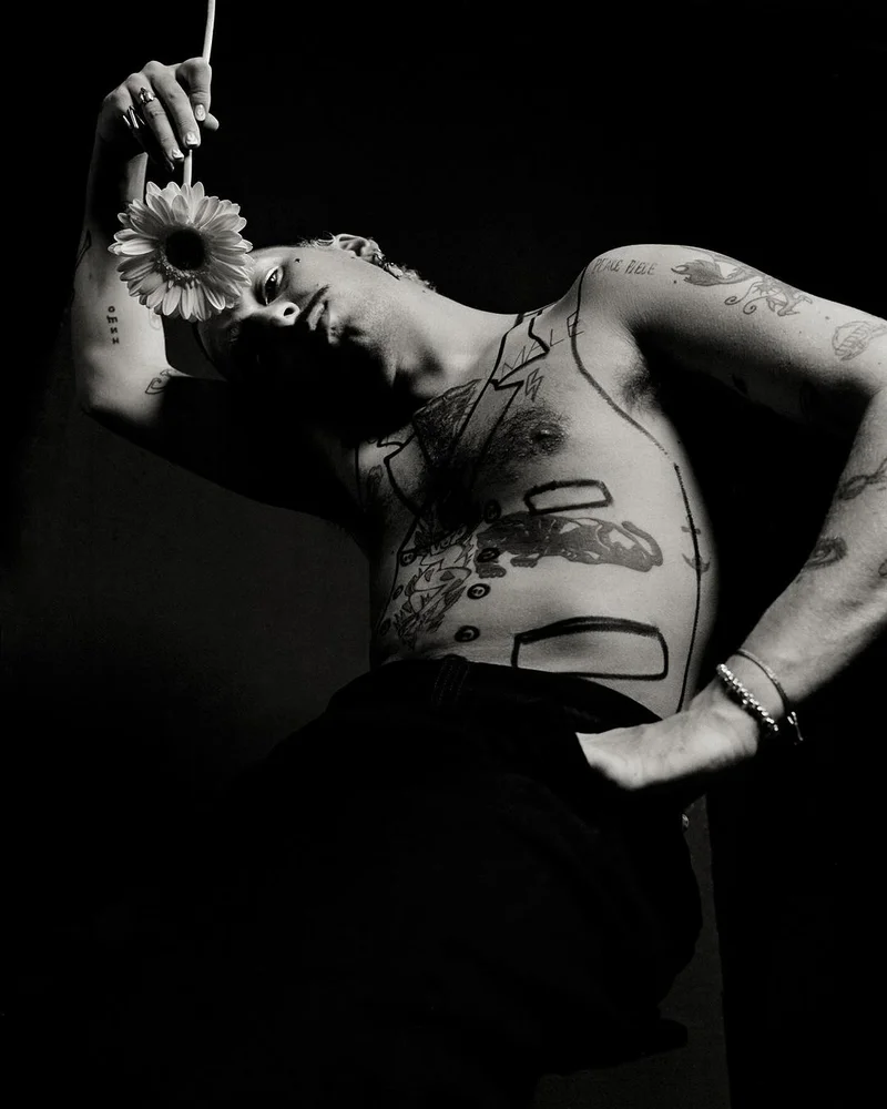 Monochrome portrait of a shirtless tattooed man holding a daisy flower above his head by photographer Andy Massaccesi