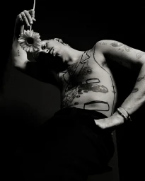 Monochrome portrait of a shirtless tattooed man holding a daisy flower above his head by photographer Andy Massaccesi