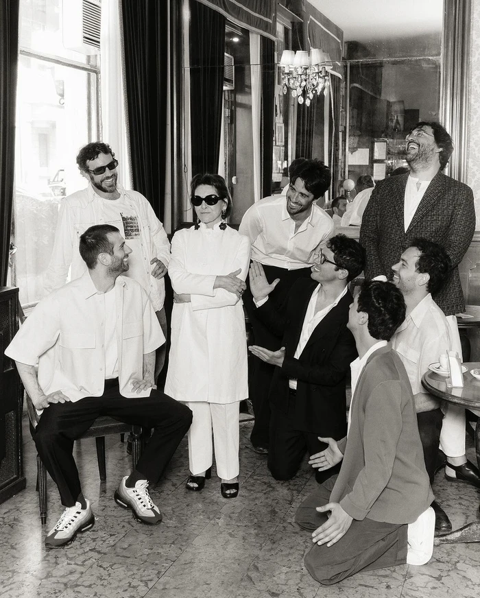 Monochrome portrait of a group of people gathered in an interior cafe setting with ornate mirrors and marble flooring by Andy Massaccesi