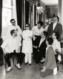 Monochrome portrait of a group of people gathered in an interior cafe setting with ornate mirrors and marble flooring by Andy Massaccesi