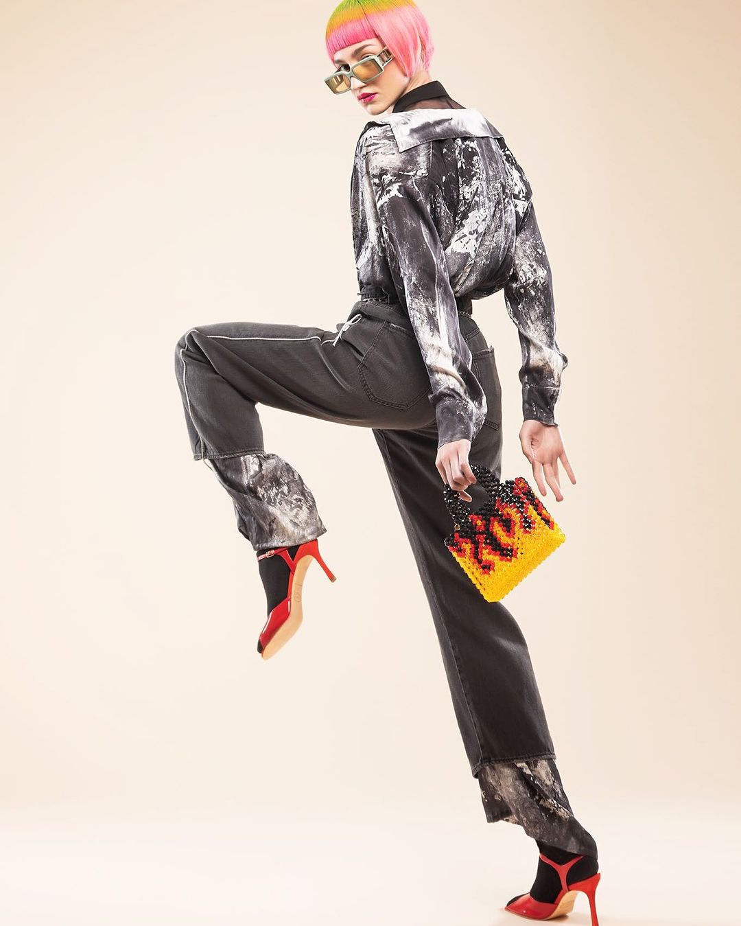 A fashionable adult female model with dyed rainbow hair is striking a pose in a studio, wearing a black and white shirt and dark pants.