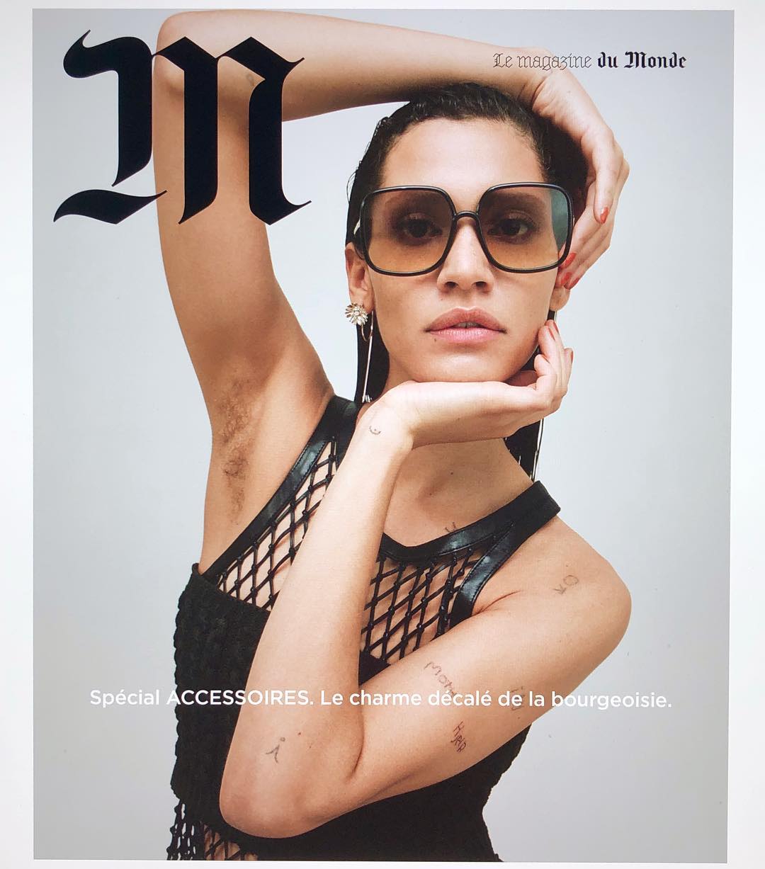 Magazine cover featuring a woman with sunglasses and a black top, posing with her hands near her face against a light background.