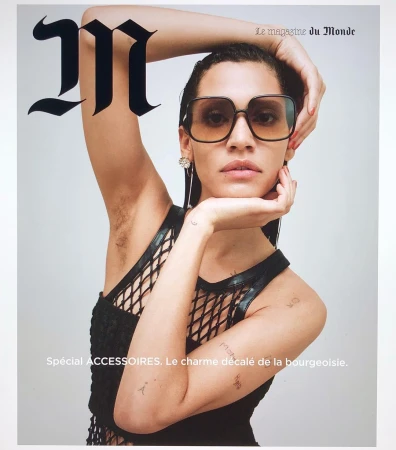 Magazine cover featuring a woman with sunglasses and a black top, posing with her hands near her face against a light background.