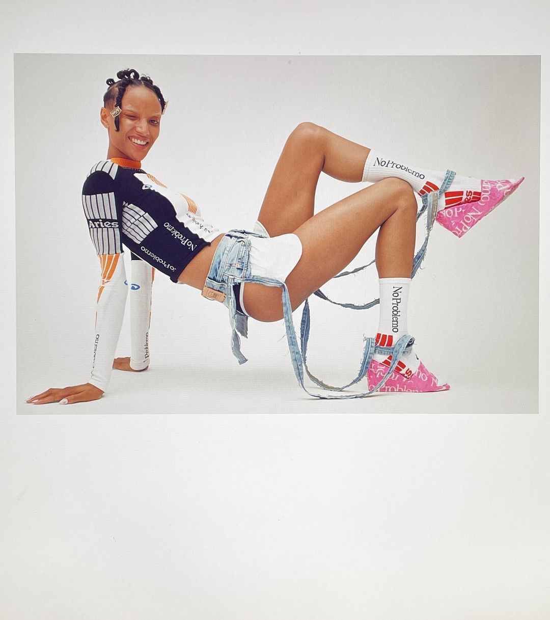 Smiling woman wearing a black and white long-sleeve shirt, denim shorts, pink shoes, and white socks posing in a studio.