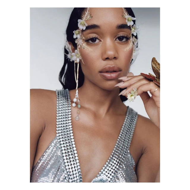 Close-up shot of a woman with flowers and beaded jewelry. She wears a silver top and has fair skin and long dark hair.